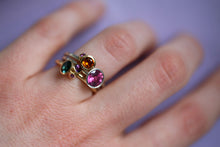 Lade das Bild in den Galerie-Viewer, Hand mit lilanem Hintergrund. Der Ringfinger hat drei verschiedene Bouquet Ringe angesteckt aus 750er/18k fairem Gelbgold, 925er fairtrade Sterlingsilber und verschiedenen fairen Steinen: Citrin, Turmaline, Amethyst, royal purple Granat und Saphir.