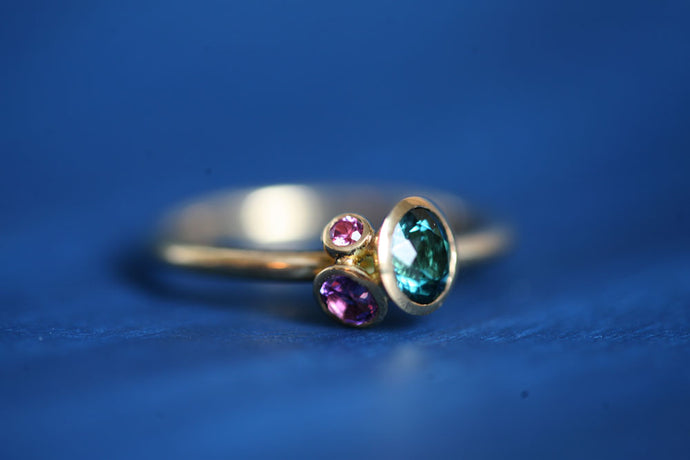 Ring aus 750er/18k fair gehandeltem Gelbgold mit Schalenfassungen in denen ein grün-blauer Turmalin, ein Amethyst und ein royal purple Granat gefasst sind.